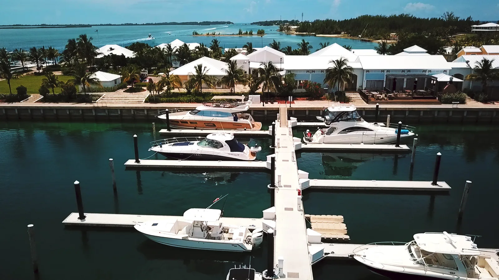 Yachts docked at Fisherman's Village marina at Resorts World Bimini, with waterfront villas and palm trees behind the docks