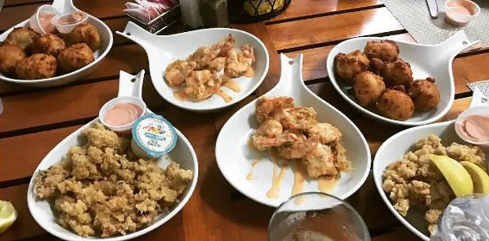 A spread of fried conch fritters, cracked conch, and conch salad served on boat-shaped plates at Bimini Seafood Company & Conch Bar