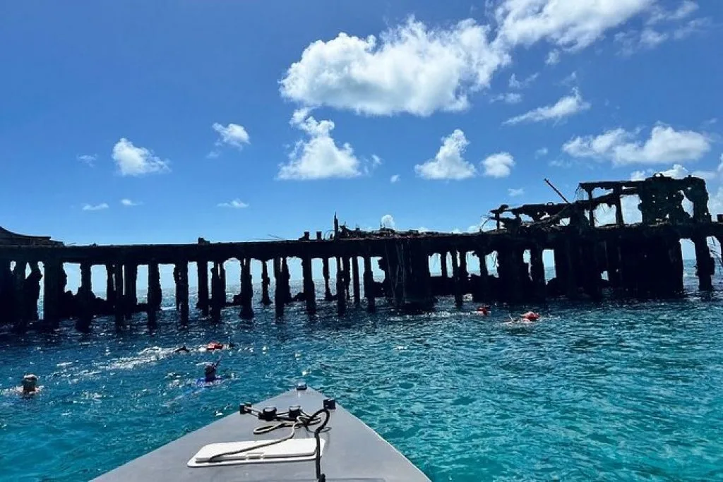 A boat approaching the pilings of a shipwreck with snorkelers in the water, on an Eclipse wreck tour near Bimini