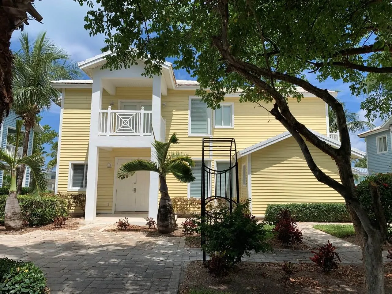 Exterior of the yellow, two-story Bimini Paradise vacation home with a covered balcony and palm trees