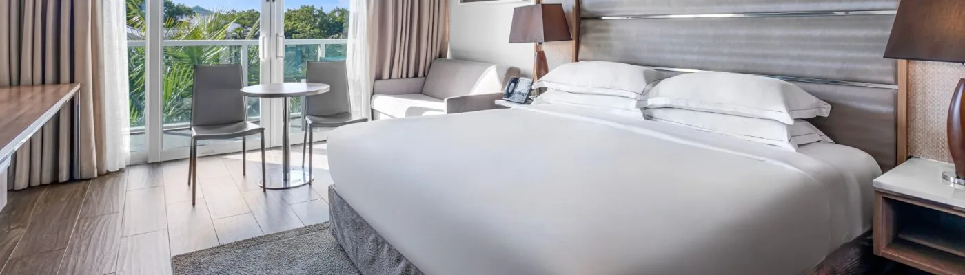A modern hotel guest room at Resorts World Bimini with a king bed, balcony, and palm-tree view